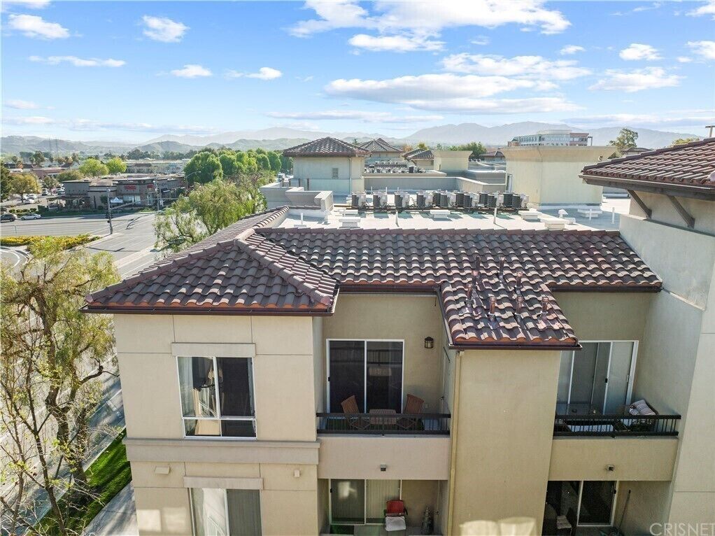 A multi-story residential building with a tiled roof, balconies, and a view of a street and mountains in the background.