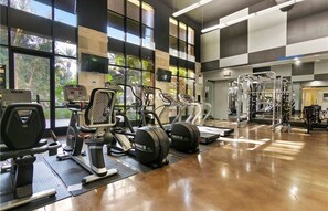 A gym with cardio machines, weightlifting equipment, and large windows offering natural light.
