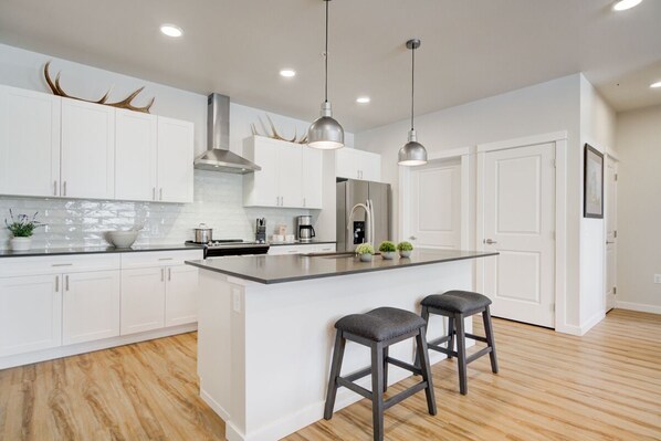 A modern kitchen with white cabinetry, a large island, stainless steel appliances, and pendant lighting.