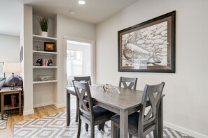 A dining area with a wooden table and chairs, a bookshelf with decorative items, and a framed artwork on the wall.