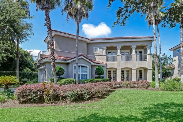 A large, two-story house with a red-tiled roof, multiple windows, and a well-maintained garden with various plants and a lawn. - Spectacular Home, 3 bed/3 bath, Private, Steps to the Ocean! Amenities (Fernandina Beach)