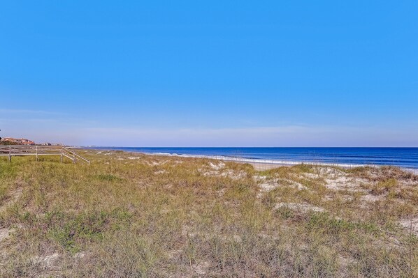 A beach with a wooden walkway leading to the water, sandy dunes, and a clear blue sky.