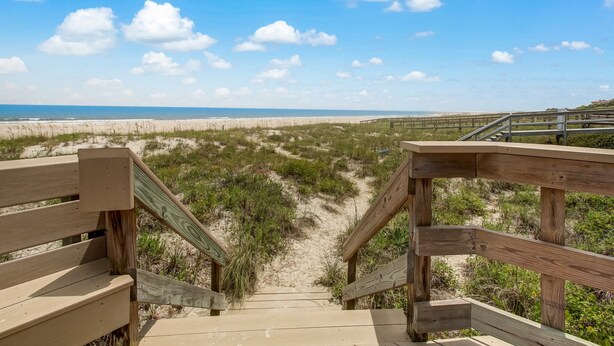 Un escalier en bois menant à une plage, avec un ciel dégagé.