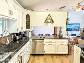 Una cocina con armarios blancos, una isla central, lavavajillas integrado y una zona de comedor con sillas.