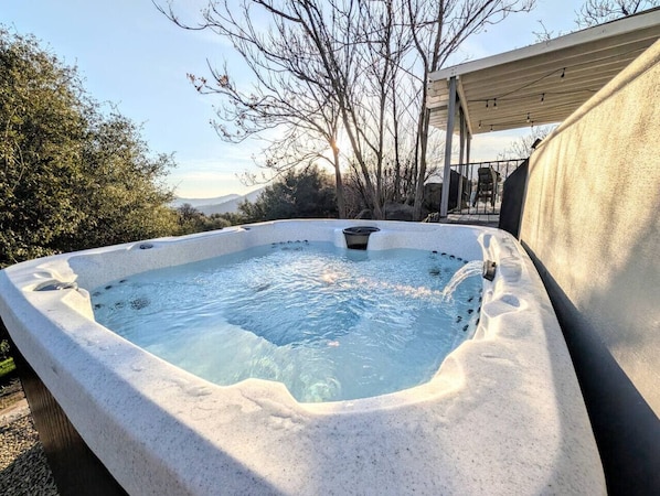 Ein Whirlpool mit Steinfassade, umgeben von Bäumen und wolkenlosem Himmel.