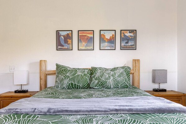 Une chambre à coucher avec un lit, deux tables de chevet, une lampe et quatre affiches encadrées accrochées au mur.