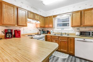 Cocina compacta con armarios de madera, estufa, microondas y cafetera.
