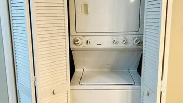 A compact, white laundry room with a built-in washer and dryer, featuring a small storage space below.