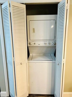 Une petite buanderie blanche, dotée d’un lave-linge et d’un sèche-linge encastrés, et comprenant un petit espace de rangement en dessous.
