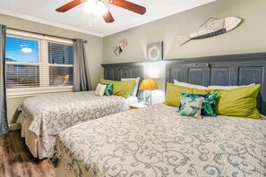 Une chambre avec deux lits, un ventilateur de plafond, une fenêtre avec des stores et une horloge murale.