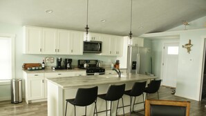 A modern kitchen with white cabinets, a central island with bar stools, stainless steel appliances, and pendant lighting.