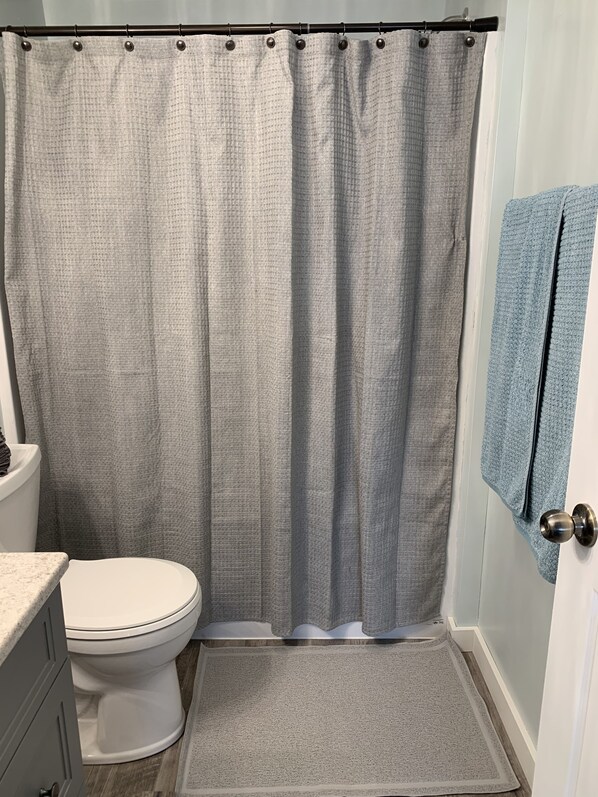 Un baño con cortina de ducha, inodoro y una toalla colgada en la puerta.