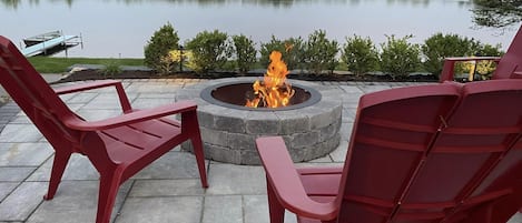 A fire pit with chairs on a patio overlooking a lake.