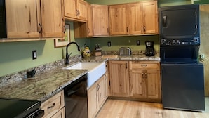 A kitchen with wooden cabinets, a granite countertop, a black refrigerator, and a coffee maker.