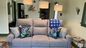 A grey sofa with floral and patterned cushions, a small side table, and a lamp.