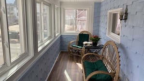 A sunlit room with large windows, wicker furniture, and a view of a house outside.