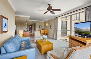 Habitación de hotel con sofá, sillón, mesa de centro, televisor y ventilador de techo.