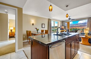Una cocina moderna con una isla grande, un comedor con sillas y vistas al paisaje a través de amplios ventanales.
