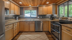 A modern kitchen with wooden cabinets, stainless steel appliances, and a large window providing a view of the outdoors. - The Treehouse at Cedar Falls by Innsbrook Vacations! (Innsbrook)