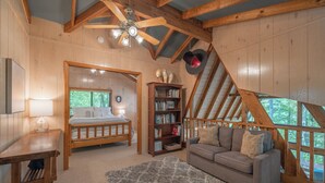 A cozy attic bedroom with a wooden ceiling, a bed, a sofa, a bookshelf, and a view of the outdoors. - The Treehouse at Cedar Falls by Innsbrook Vacations! (Innsbrook)