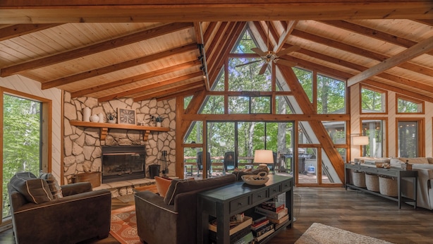A spacious living room with a stone fireplace, wooden beams, large windows, and a cozy seating area. - The Treehouse at Cedar Falls by Innsbrook Vacations! (Innsbrook)