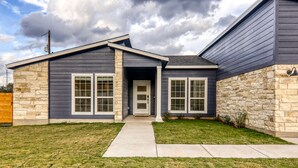 A modern two-story house with a stone facade, a front door, and a small front yard. - Hill Country Retreat | Hot Tub | Fire Pit (Lago Vista)