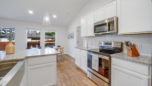 A modern kitchen with white cabinetry, stainless steel appliances, and a granite countertop. - Hill Country Retreat | Hot Tub | Fire Pit (Lago Vista)