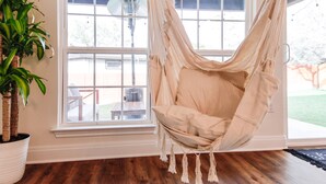 A hammock chair in a room with wooden flooring, large windows, and a potted plant. - Hill Country Retreat | Hot Tub | Fire Pit (Lago Vista)