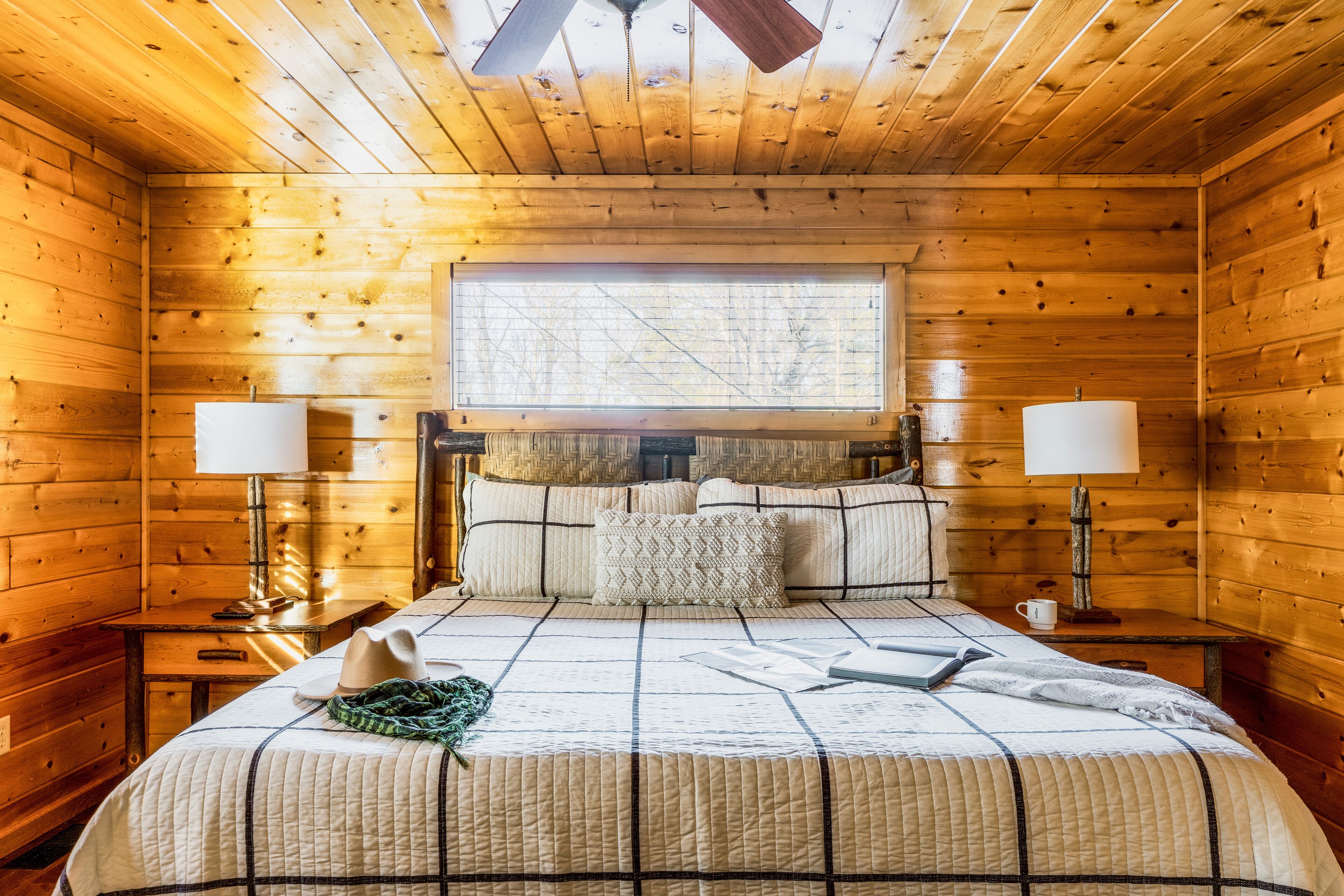 Ein Schlafzimmer einer Holzhütte mit einem Bett, zwei Nachttischlampen, einem Fenster und einem Deckenventilator.