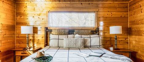 Ein Schlafzimmer einer Holzhütte mit einem Bett, zwei Nachttischlampen, einem Fenster und einem Deckenventilator.