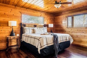 Un dormitorio rústico de cabaña de madera con una cama, dos mesitas de noche y un ventilador de techo.