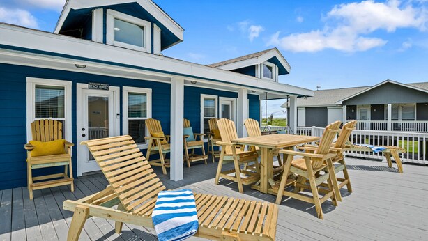 Una casa de playa con un porche techado, mobiliario exterior y un letrero que indica que es una casa de playa.