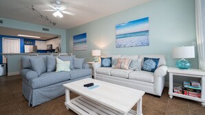 A living room with two sofas, a coffee table, and a TV. There are paintings on the wall and a ceiling fan. - Million-Dollar Gulf Views • Majestic Beach Resort 504 Tower 1• Beachfront • Pool (Panama City Beach)