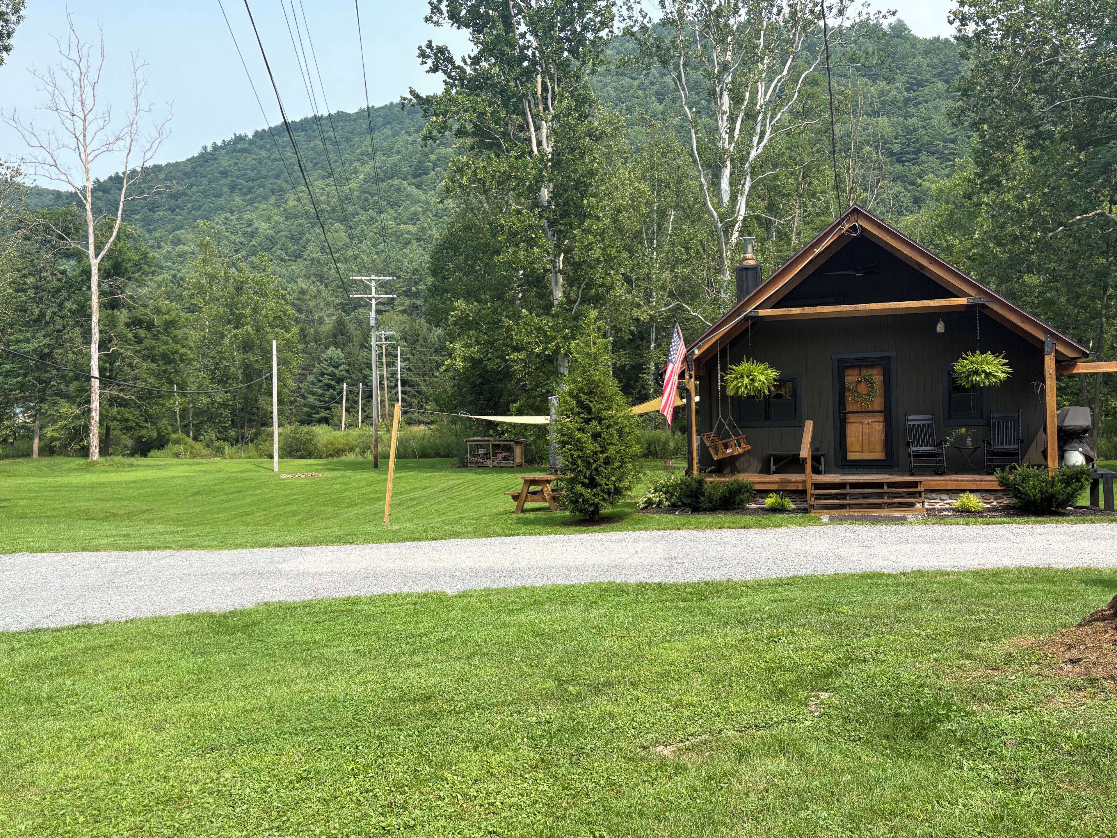 A cabin with a porch, outdoor seating, and a view of a forested hill.