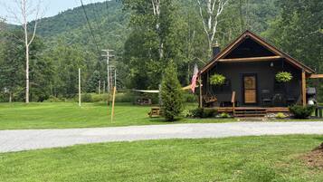 A cabin with a porch, outdoor seating, and a view of a forested hill.
