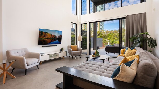 A modern living room with a sofa, armchairs, and a coffee table. There is a TV mounted on the wall and a large window providing a view of the city. - Stunning Waterfront Home in Surfers Paradise.
Heated Pool and Pet Friendly (Surfers Paradise)