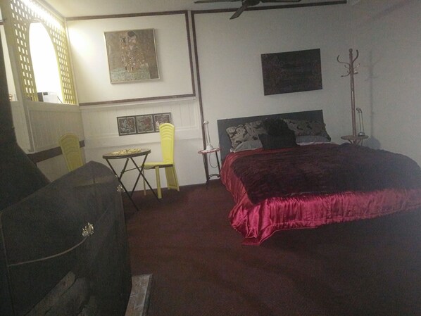 Une chambre avec un grand lit, une petite table, une chaise et un porte-manteau.