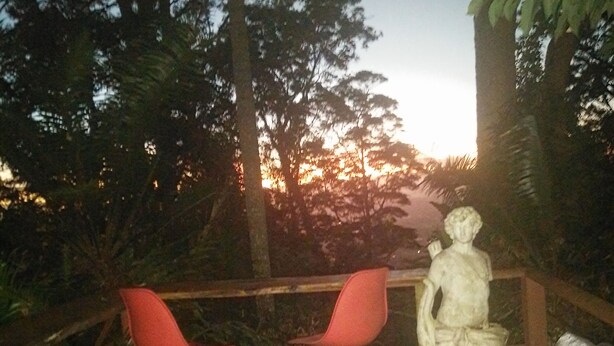 An outdoor seating area with two red chairs and a statue, surrounded by trees and a sunset in the background. - Rainforest setting with sunset views (Tamborine mountain)