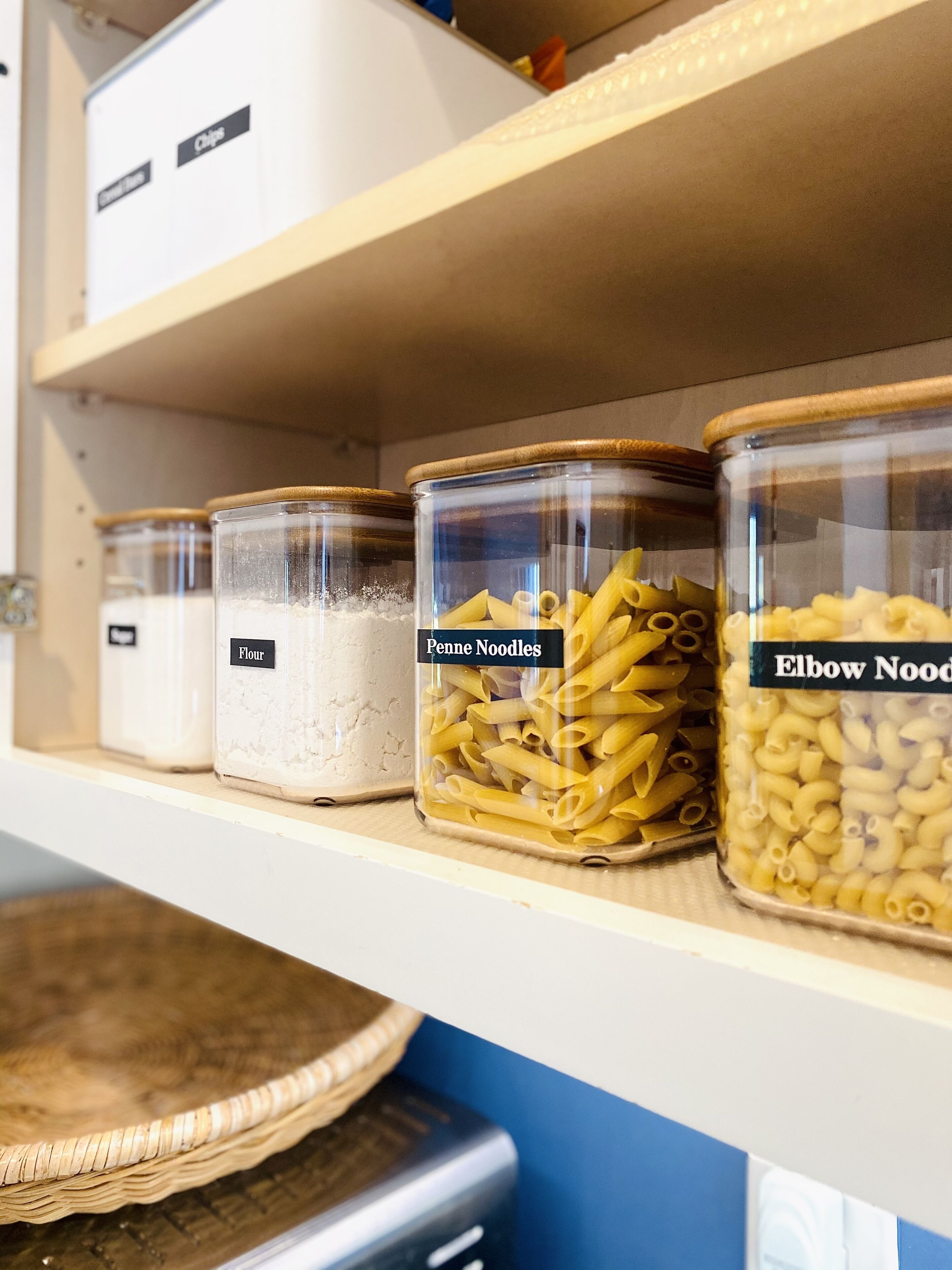 En hylla med märkta behållare innehållande olika sorters pasta, inklusive mjöl, penne och makaroner.