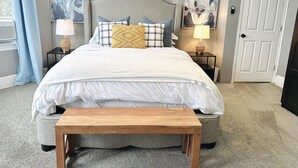 A bedroom with a bed, two bedside tables, a bench, and two paintings on the wall. - Your Family Friendly Home with Large Backyard & Onsite Parking (New Rochelle)