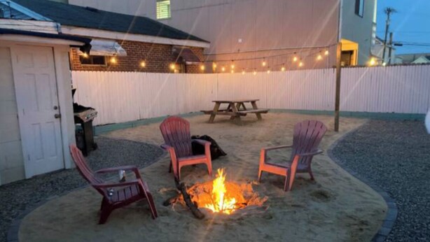 Un patio al aire libre con un hogar para fuego, cuatro sillas Adirondack y luces colgantes.