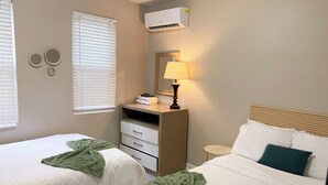 Habitación de hotel con dos camas, una mesita de noche con lámpara, cómoda y aire acondicionado.