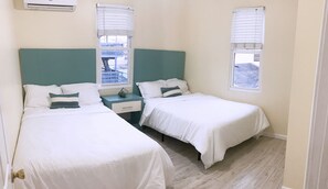 Habitación doble con dos camas individuales, una mesita de noche pequeña con lámpara y una ventana con persianas.
