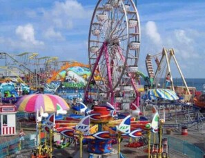 Un parque de atracciones colorido con diversas atracciones y juegos, incluyendo una noria y un carrusel.