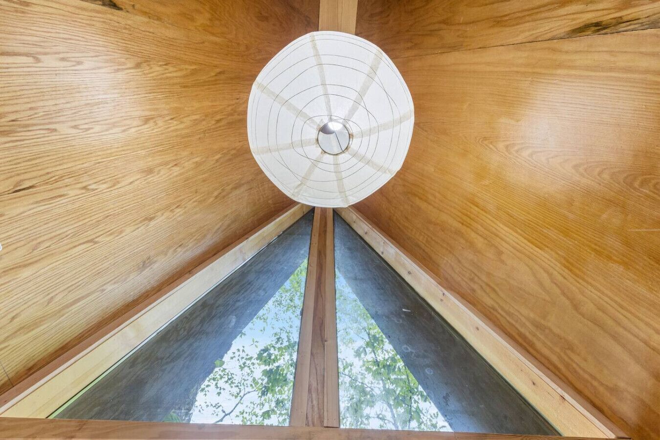 Ein Holzinnenraum mit einem zentralen runden Element an der Decke und Blick auf Bäume durch ein Fenster.