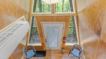 A cabin with a loft bedroom, two windows, a door, a fire extinguisher, and a small table with chairs.