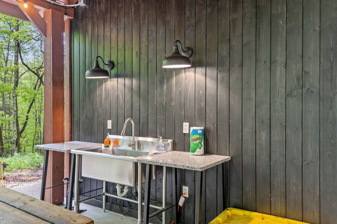 A rustic outdoor kitchen with a sink, two wall-mounted lights, and a Bounty dish soap bottle.