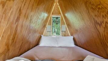 A cozy, wooden tent-style room with a bed, pillows, and a view of greenery outside.