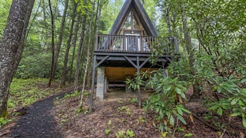 A cabin in a forest with a wooden deck and a dirt path leading to it.