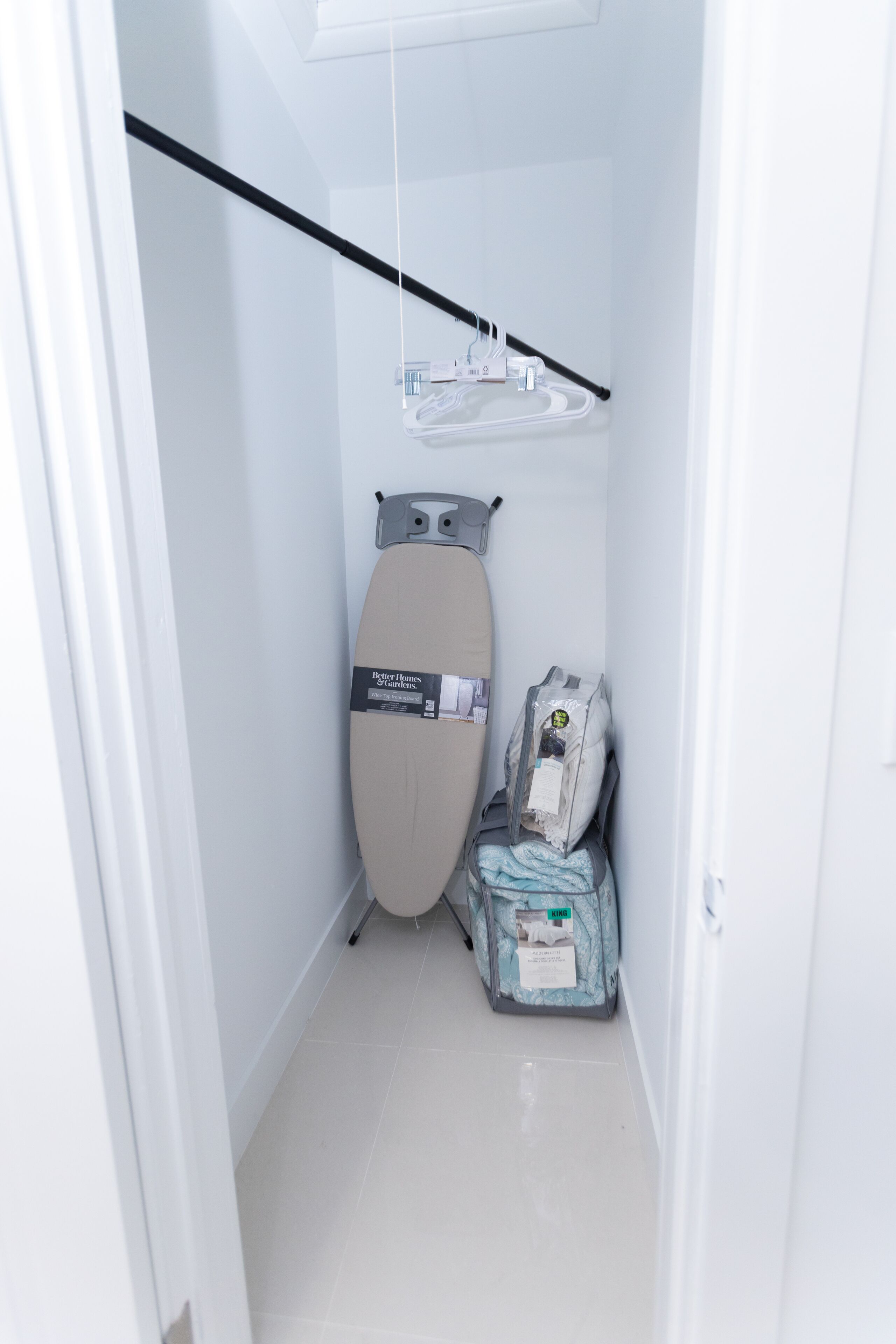 Un couloir étroit avec un fer à repasser fixé au plafond, un étendoir mural et un sac de linge sale.